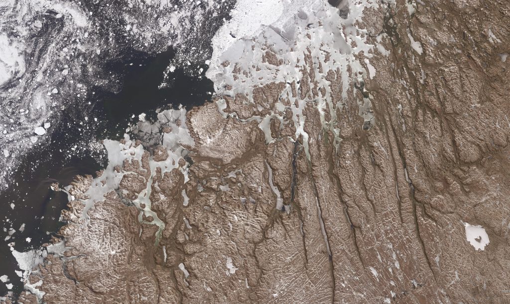 Jay Hart&nbsp;• <em>Mistastin and the Fraser Canyons</em>&nbsp;• Inkjet print of Landsat imagery&nbsp;• 37″×&nbsp;22″&nbsp;• $400.00<div class="fb-text&quot><p style="margin-top:5px; text-align:center; font-size: 0.8em; ">North America's east coast has a strong modifier in its offshore current, the Gulf Stream. Its warmth has lessened the effects of increasing latitude for many millennia in the last million years. There is strong evidence that the effect (and the current) shuts down at the onset of the cold portions of our cycle; it could be our saving grace in this global spiking of temperatures. Here in June 2014 is the north shore of Labrador, a fortnight away from the summer solstice, with a light covering of fresh snow tracing every rumple. Straight valleys were born of meltwater draining from the continental ice dome to the west, across a hard and probably ice-leveled rock surface. The prominent lake of the title is a 35 million year old impact crater.</p></div>