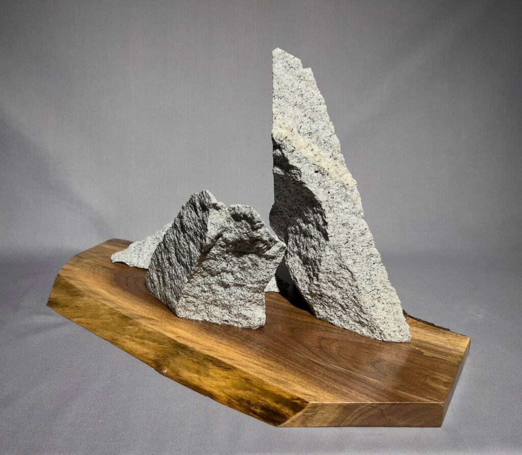 Eva M. Capobianco&nbsp;• <em>Granite Trio</em>&nbsp;• Curb pieces on walnut slab&nbsp;• 19″×&nbsp;11″×&nbsp;11″&nbsp;• $475.00